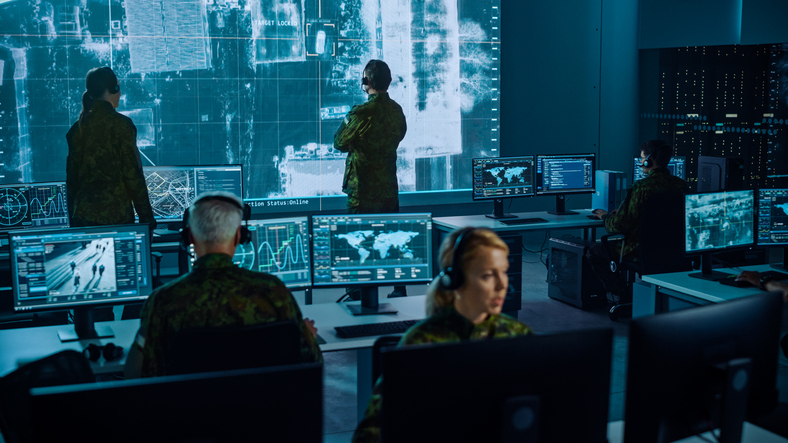 A Global Security Operations Center where various operators look at computer screens and a large video wall simultaneously.