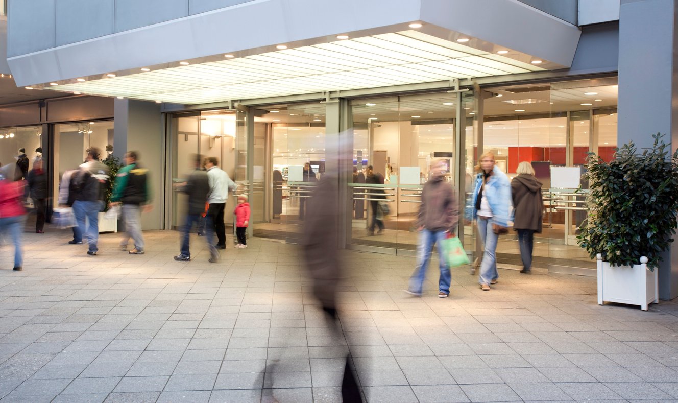 retail store entrance shows blurry shoppers walking by with focus on doors of the store